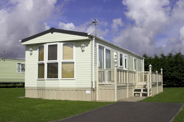 A mobile home with a porch and grassy area, under a cloudy sky.