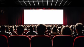 An audience seated in a theater facing a blank screen with red curtains.