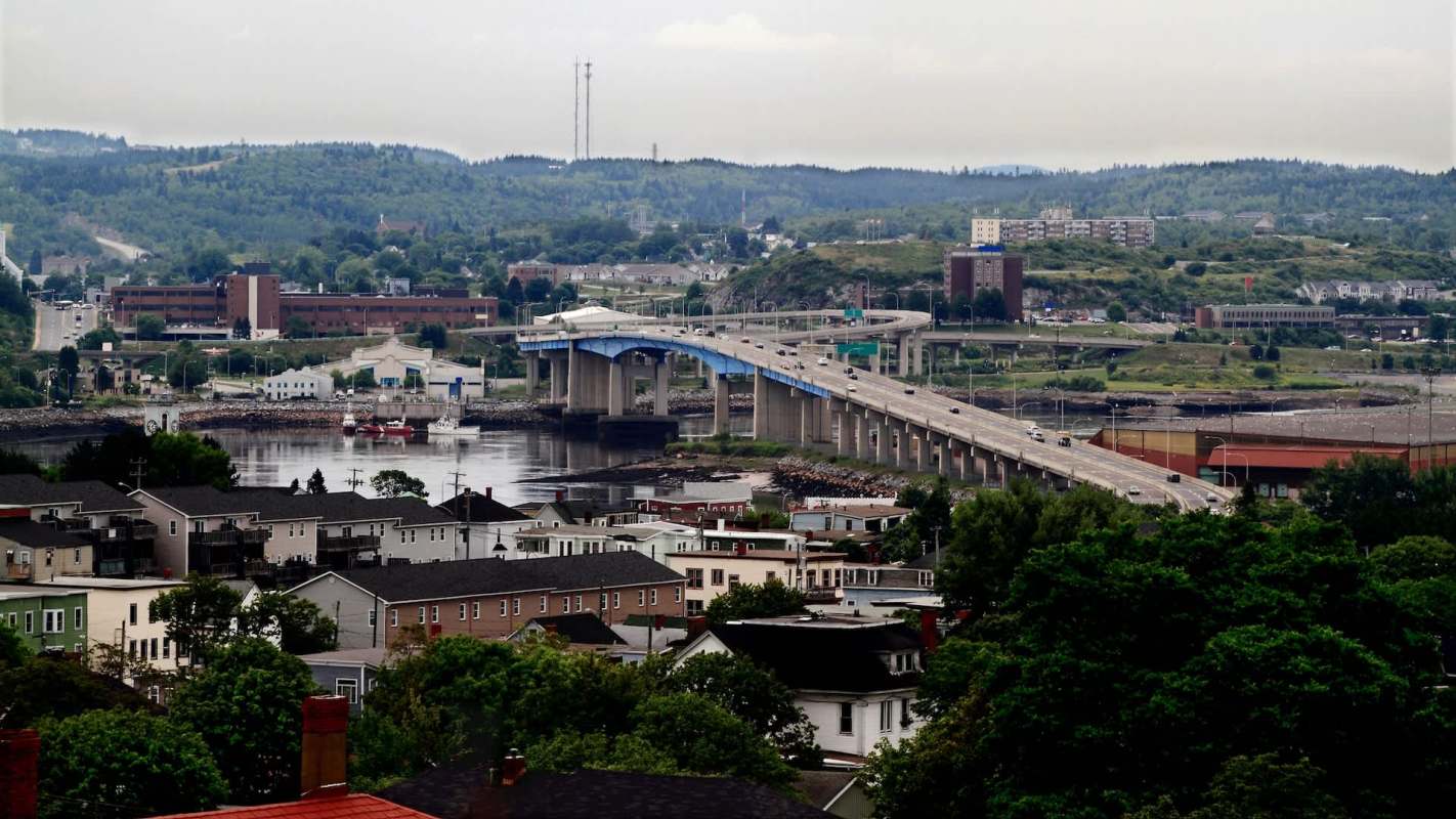A view of a Saint John, New Brunswick, Canada, with a bridge spanning across a river and various buildings and hills in the background.
