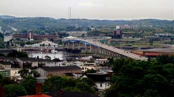 A view of a Saint John, New Brunswick, Canada, with a bridge spanning across a river and various buildings and hills in the background.