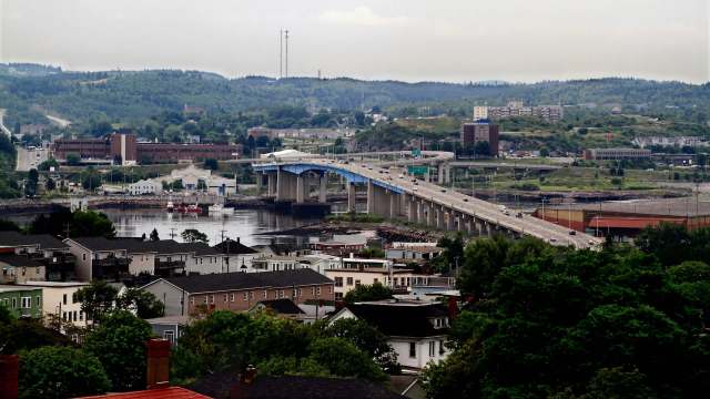 A view of a Saint John, New Brunswick, Canada, with a bridge spanning across a river and various buildings and hills in the background.