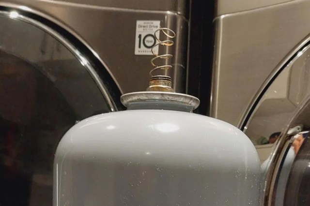 A gray tank with a coiled metal spring on top, placed near washing machines.