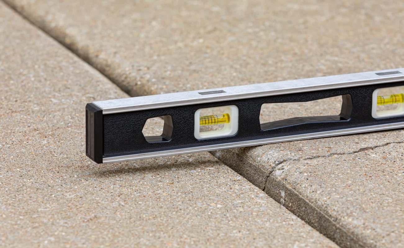 A level tool is placed on a concrete surface with visible cracks.
