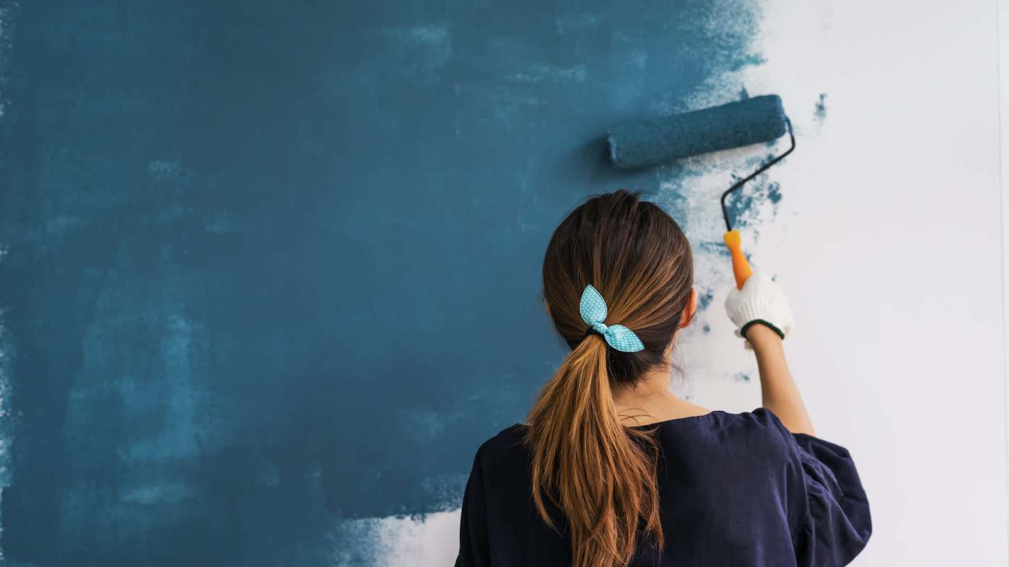 A person paints a wall with a blue roller in a room.