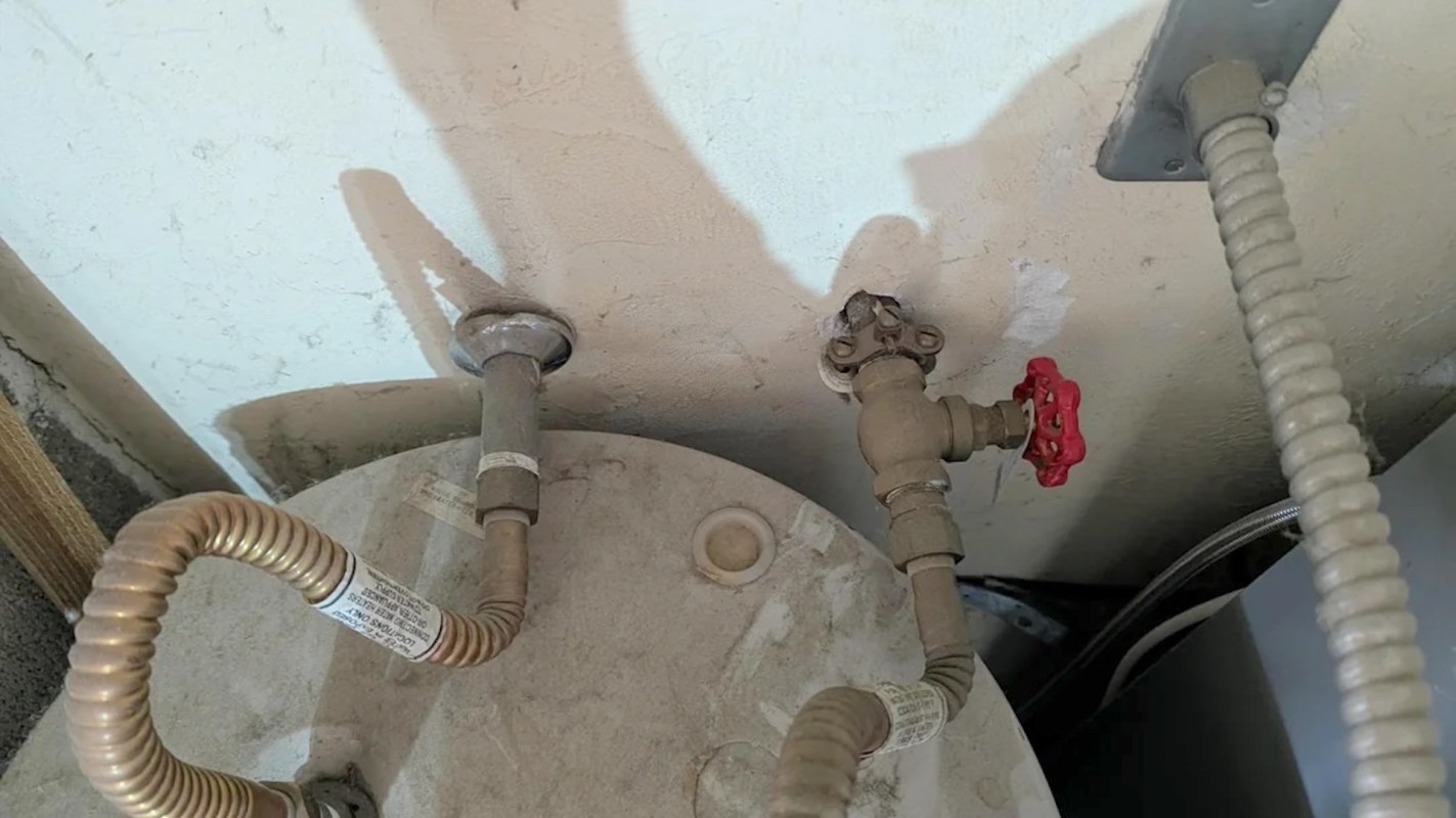 A water heater with pipes and valves, including a red valve and visible labeling.
