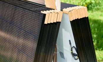 Solar panels stacked together, secured with cardboard corners, on a grassy surface.