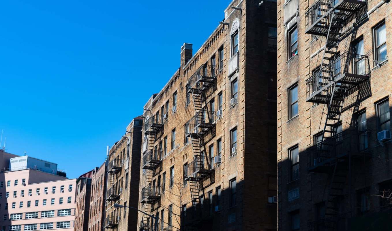 Brick buildings with fire escapes under a clear blue sky.