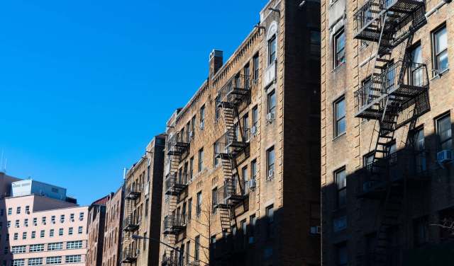 Brick buildings with fire escapes under a clear blue sky.