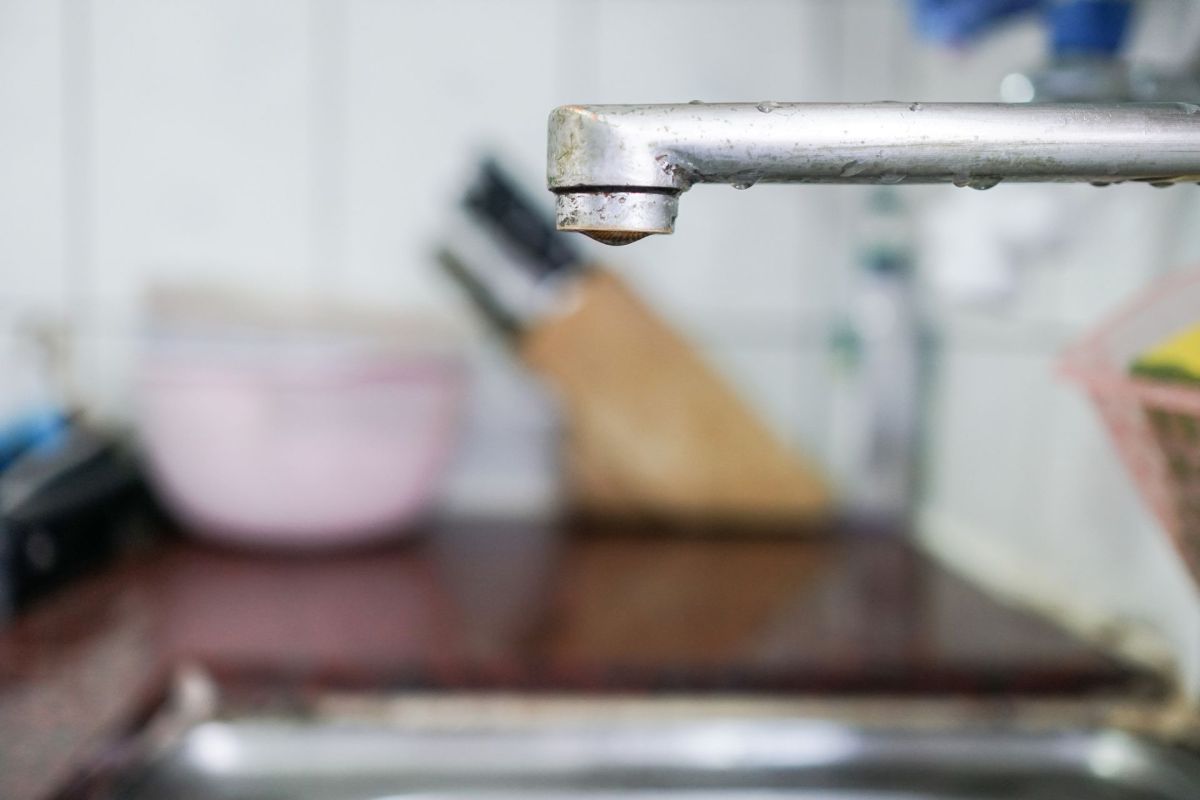 A kitchen sink faucet with a drop of water forming at the tip.