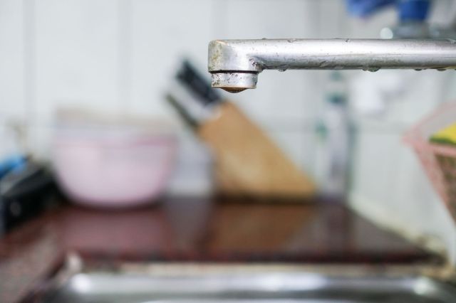 A kitchen sink faucet with a drop of water forming at the tip.