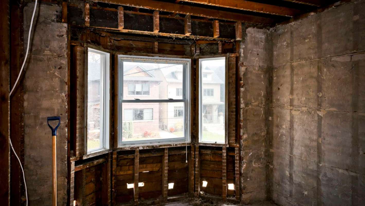 An empty room under renovation with exposed wooden beams and a large window.