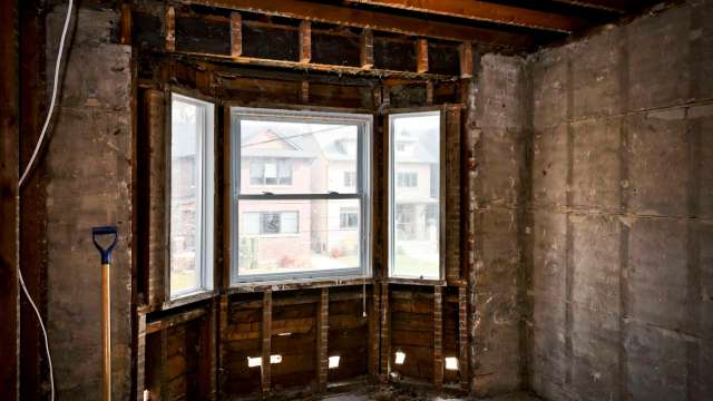 An empty room under renovation with exposed wooden beams and a large window.