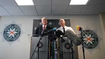 Two men stand at podiums with microphones during a press conference, with the Police Service of Northern Ireland logos in the background.