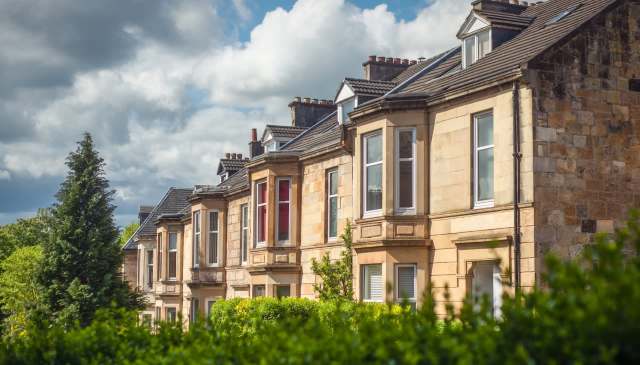Row of residential buildings with windows, greenery, and a cloudy sky in the background.