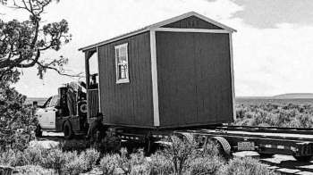 A small red house being loaded onto a flatbed truck in a rural area.