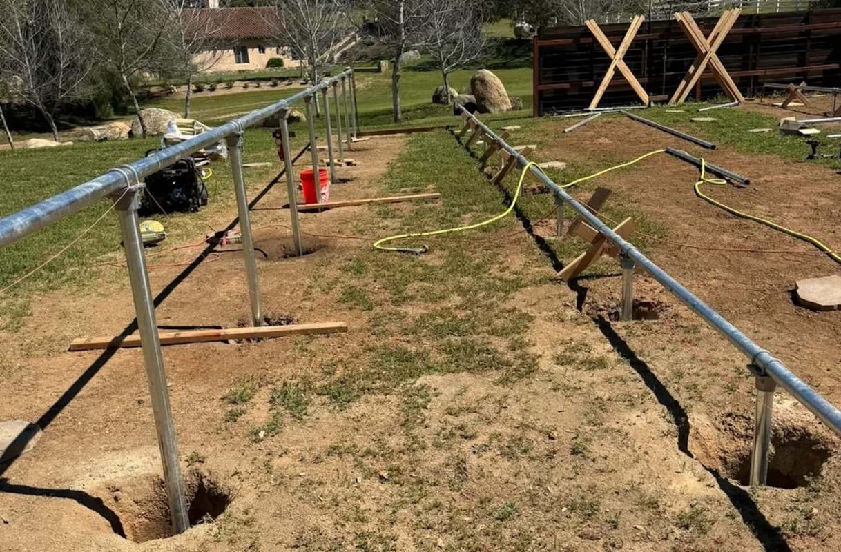 A construction site with metal poles, holes in the ground, and tools scattered on the grass.