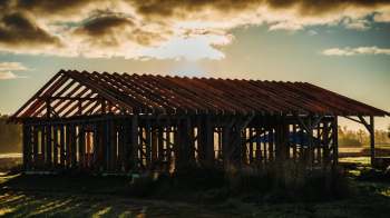 An unfinished wooden structure with a prominent roof frame under a cloudy sky.