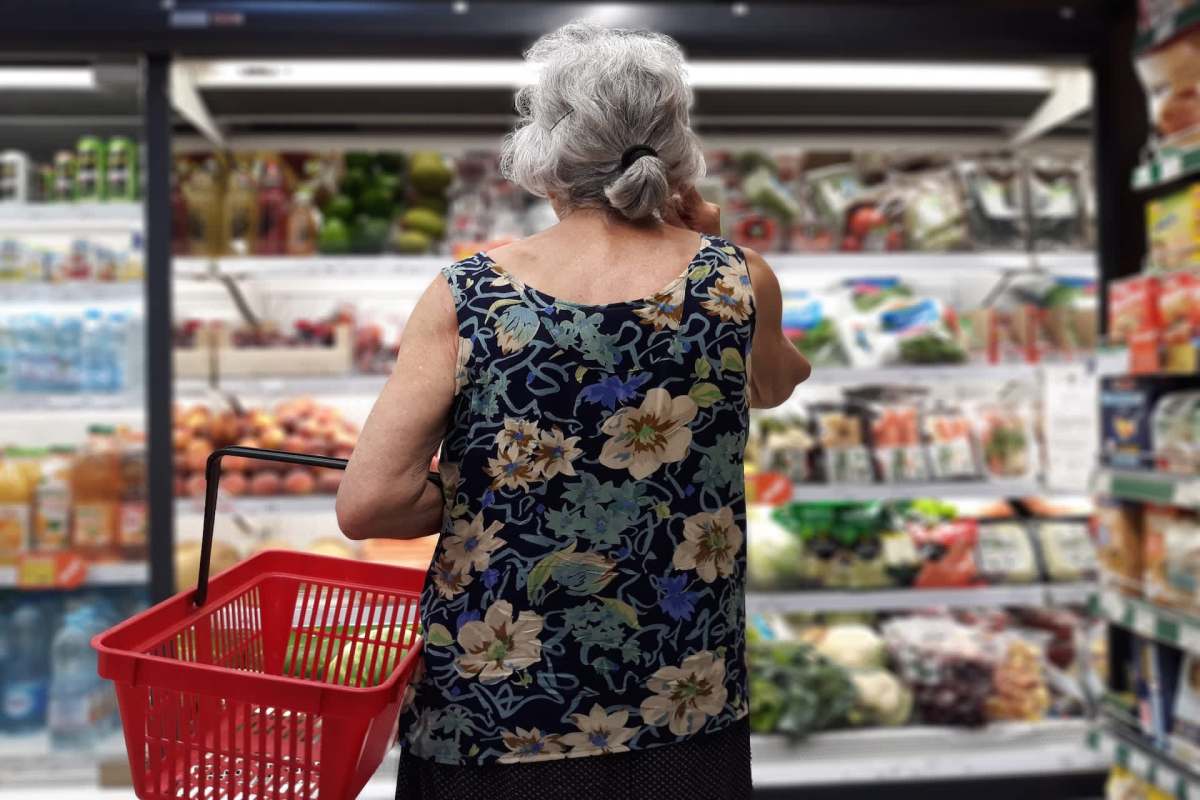 An older woman with a shopping basket in a grocery store.