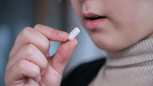 A person holds a white pill near their mouth.
