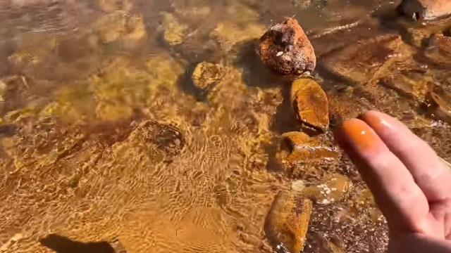 A hand has orange residue from the lake below.