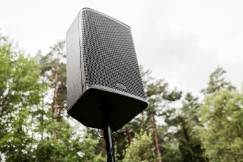 A black speaker mounted on a pole with trees in the background.