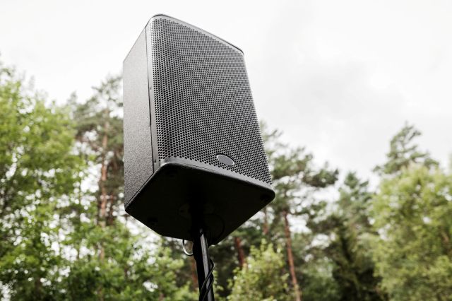 A black speaker mounted on a pole with trees in the background.