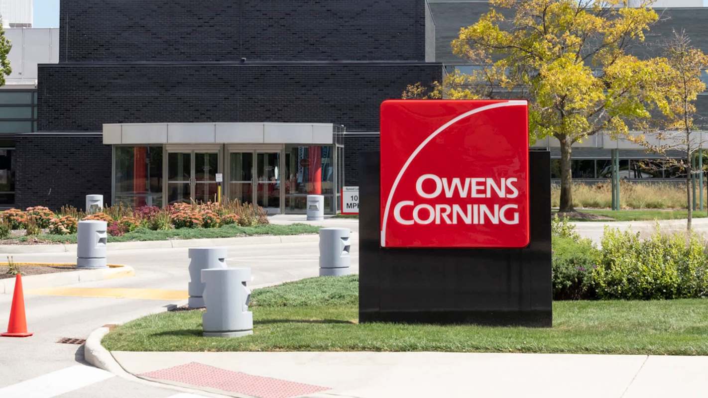 A sign for Owens Corning outside a modern building with landscaped areas and safety barriers.