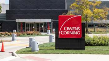 A sign for Owens Corning outside a modern building with landscaped areas and safety barriers.