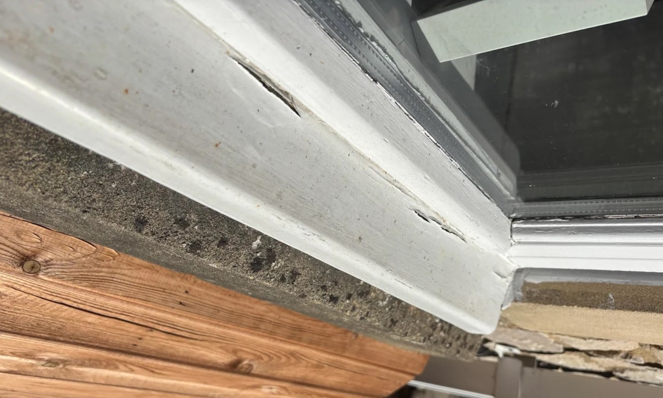 A damaged window frame showing cracks in the white paint and a wooden sill.
