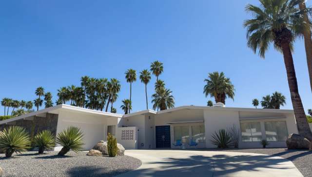 A modern white house surrounded by palm trees and desert landscaping.