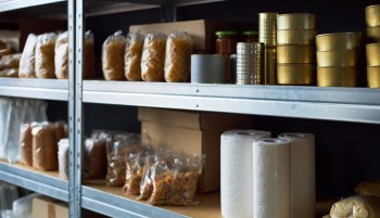 Shelves stocked with various food items, including bags of pasta, jars, canned goods, and paper towels.