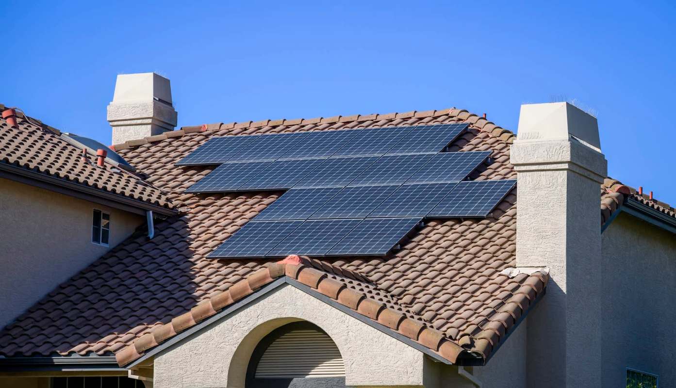 A house roof equipped with several solar panels under a clear blue sky.