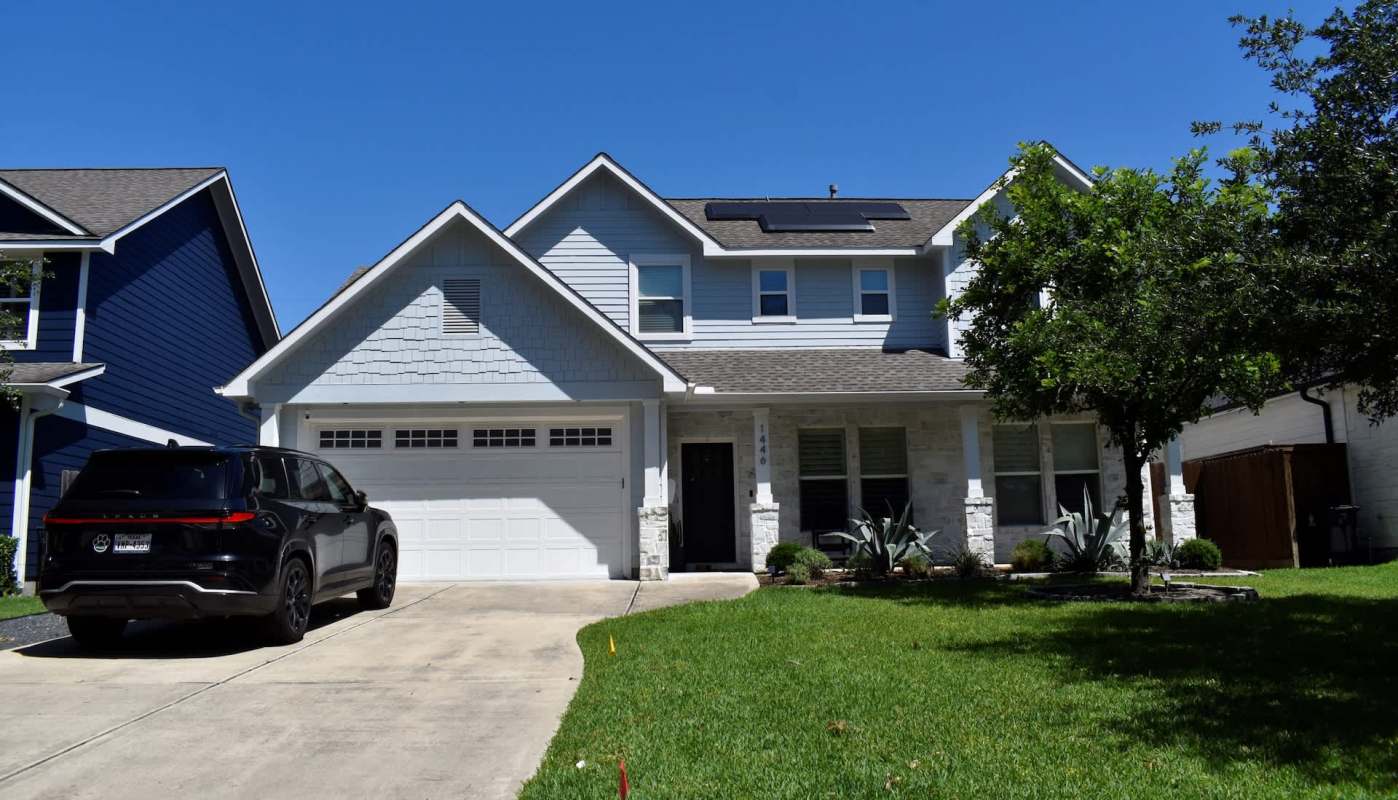 A two-story house with solar panels, a driveway, and landscaped front yard.