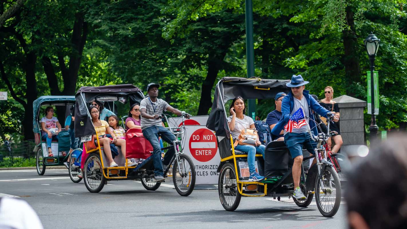 Rickshaws with passengers ride past a "Do Not Enter" sign in a park.