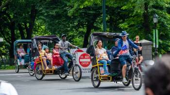 Rickshaws with passengers ride past a "Do Not Enter" sign in a park.