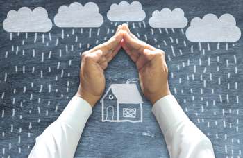 Hands forming a roof over a chalkboard drawing of a house in a storm.