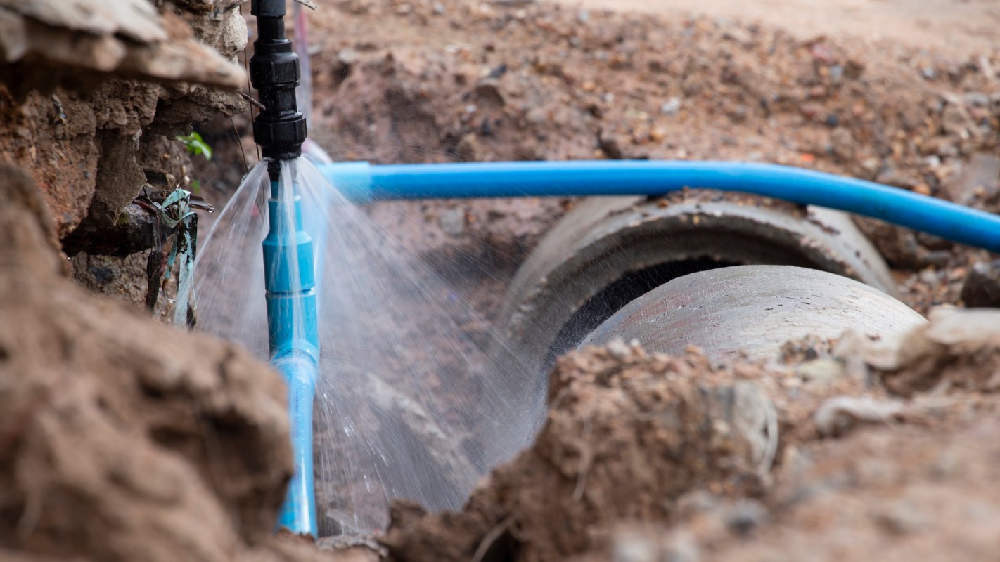 A blue irrigation pipe spraying water surrounded by soil and rocks.