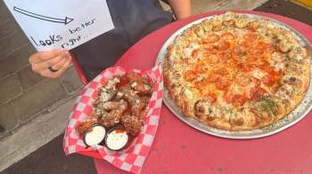 A pizza with pepperoni and a basket of chicken wings with dipping sauces on a red table.