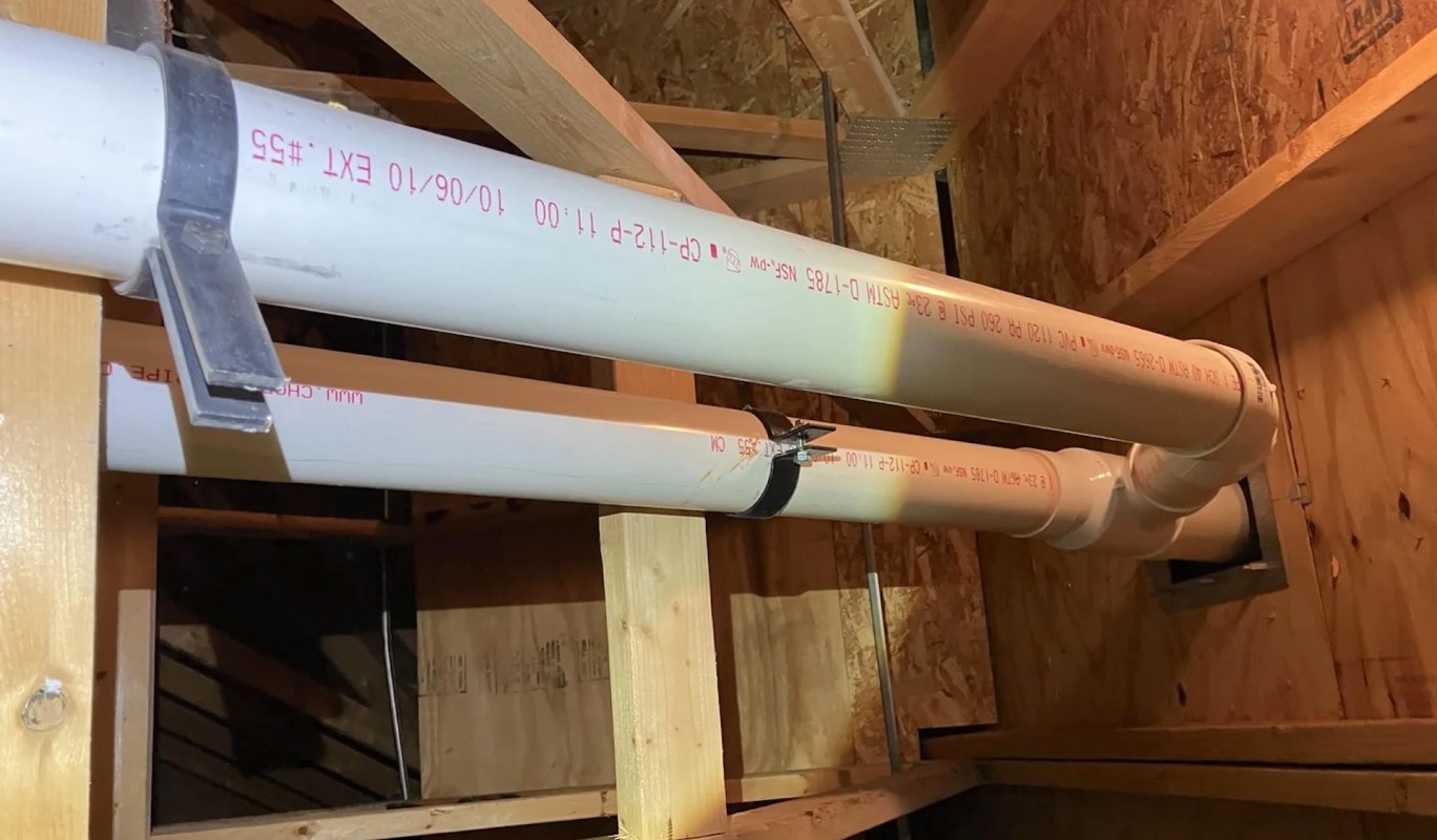 Two PVC pipes secured with brackets in a wood-framed structure.