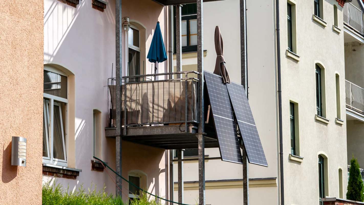 A balcony with a blue umbrella and a solar panel, surrounded by adjacent apartment buildings.