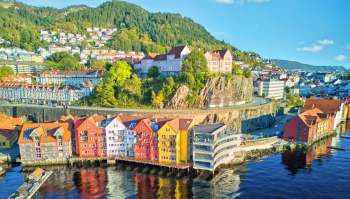 A view of colorful waterfront buildings with hills and trees in the background.