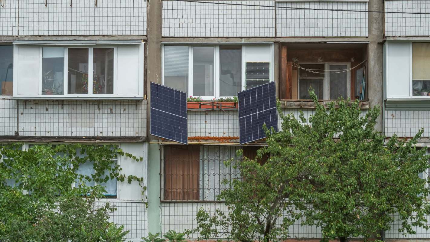 Solar panels are mounted on a balcony of an apartment building surrounded by greenery.