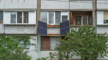 Solar panels are mounted on a balcony of an apartment building surrounded by greenery.