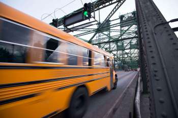 An orange school bus passes under a green traffic light on a bridge.