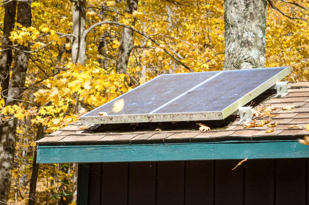 A solar panel installed on the roof of a shed surrounded by autumn foliage.