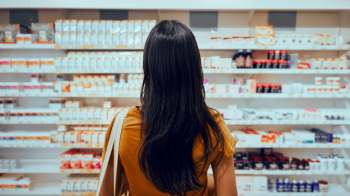 A person in a pharmacy stands in front of shelves filled with various medications and health products.