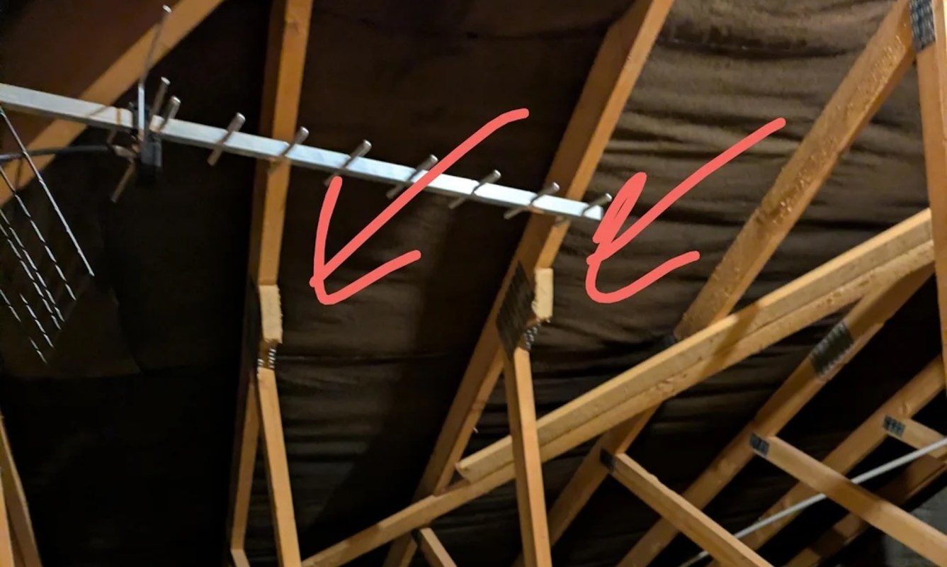 An attic with wooden trusses and arrows pointing to connection points.