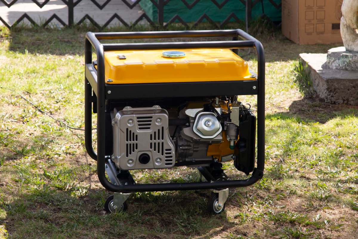 A portable generator with a yellow top and a black frame is positioned on grass.