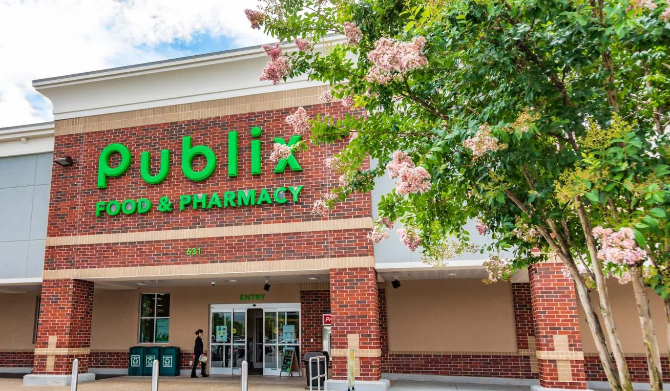 A Publix grocery store entrance surrounded by flowering trees.