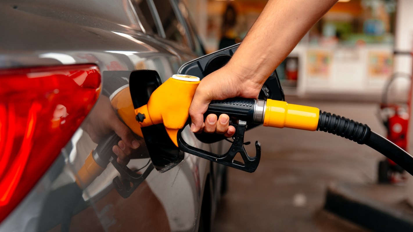 A person refuels a car using a gas pump with an orange nozzle.